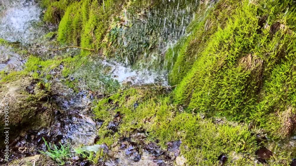 Kleiner Wasserfall an grüner moosbewachsener Felswand im Tageslicht Kleiner Wasserfall an grüner moosbewachsener Felswand im Tageslicht
