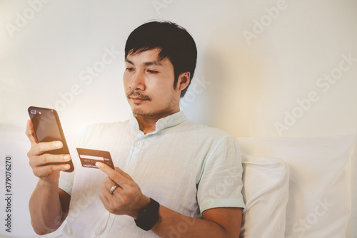 A handsome man is holding credit card and using a mobile phone shopping online. The busines is working at home. Online shopping, e-commerce, internet banking, spending money, working from home concept