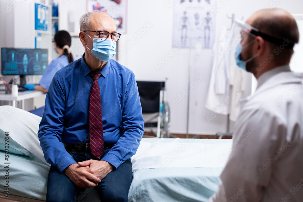 Sick patient talking with doctor during consultation wearing protective mask against covid in hospital consultation room. Global health crisis, medical system during pandemic, sick elderly patient. Sick patient talking with doctor during consultation wearing protective mask against covid in hospital consultation room. Global health crisis, medical system during pandemic, sick elderly patient.