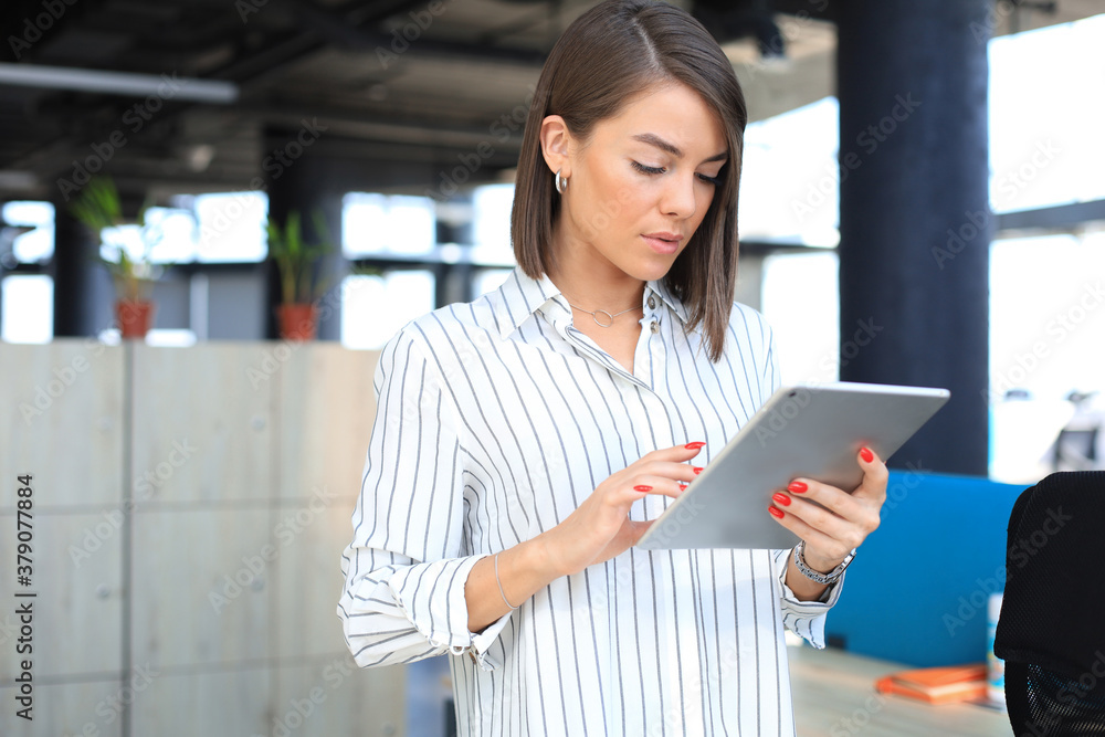 Portrait of young businesswoman looking at touch pad screen while standing in modern office space interior. Portrait of young businesswoman looking at touch pad screen while standing in modern office space interior.