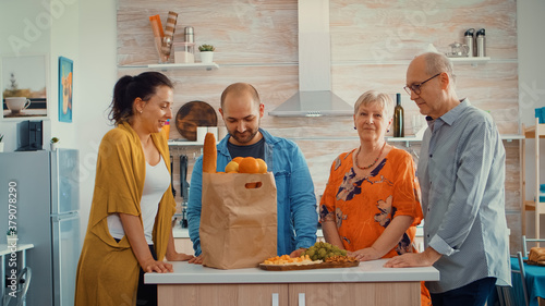 Video portrait of happy extended family smiling at the camera, sitting in the kitchen. People in dining room around the papper bag with groceries looking at the web cam photo