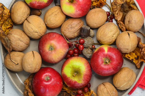 autumn decor walnuts apples rowan branch acorns on ceramic plate top view, autumn food concept