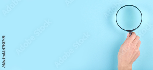 Hand with black magnifying glass on blue background. Flat lay, overhead view image. Copy space, template.