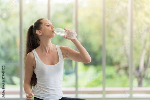 Photo of young pretty woman in sportswear drinking water and sitting doing yoga exercises at home photo