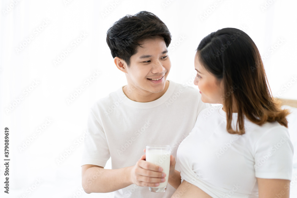 Lovely Asian couple taking care together in their house, husband taking care his pregnant wife by giving a fresh milk. Wellness and health care in pregnancy woman and unborn child in tummy. Lovely Asian couple taking care together in their house, husband taking care his pregnant wife by giving a fresh milk. Wellness and health care in pregnancy woman and unborn child in tummy.