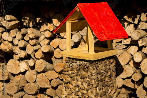 selbst gebautes vogelhaus mit roten dach vor einem stapel holz im garten