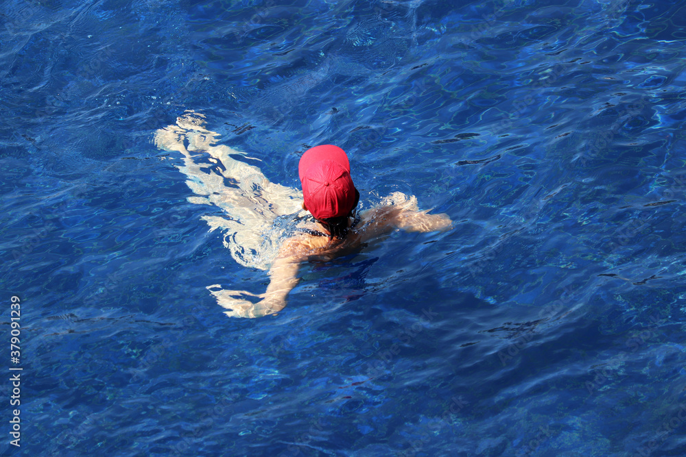 Woman in red cap swimming in the pool, top view. Relaxation on the water, beach vacations
