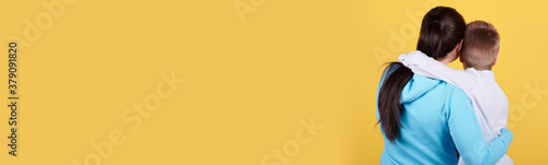 Brunette boy and mother sitting together, hugs, love, family. Isolated on yellow background, copy space template, banner.