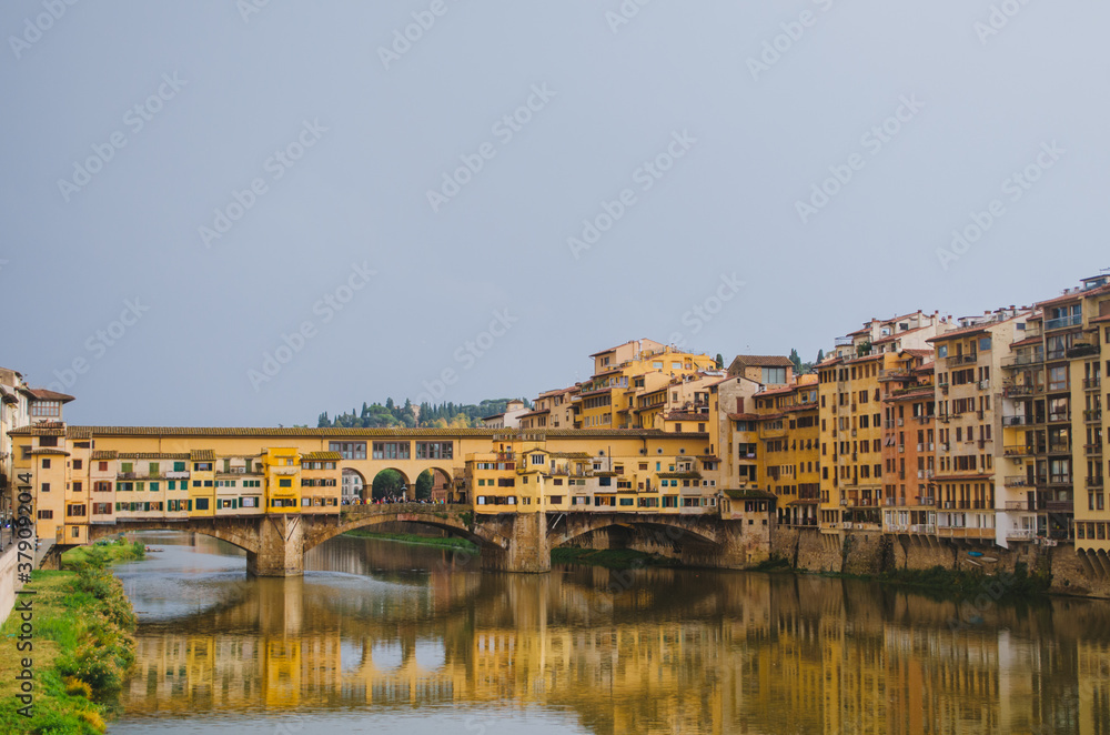 Rome, Italy - A panoramic side view of the Ponte Vecchio and the Arno river reflecting the buildings in its water during a cloudy afternoon.