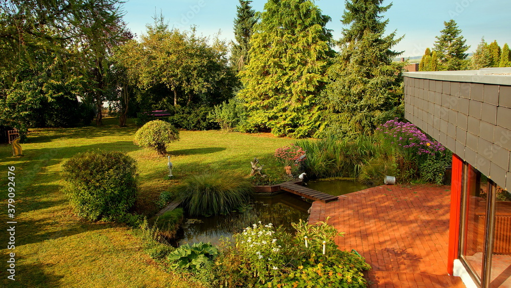 moderner Bungalow mit schöner Terrasse am Teich mit  Holzbrücke und herbstlichen Garten	