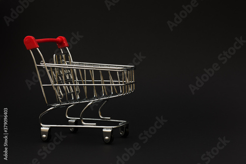 small metal trolley from the supermarket on a black background. Horizontal photo, low key photo, Copy space. Concept - sales, advertising Black Friday.
