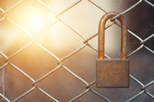 An old and rusty lock hanging on the iron mesh fence.