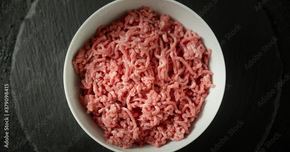 Bowl with raw minced meat slowly rotates on a stone board. Bowl with raw minced meat slowly rotates on a stone board.