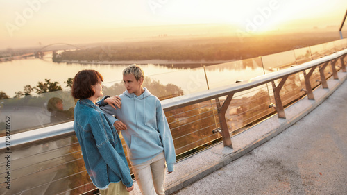 Two girls looking at each other, standing on the bridge, Young lesbian couple having romantic moment outdoors