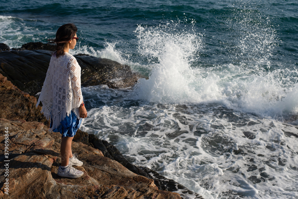 One Asian woman standing on rocks, wave crashing the shore