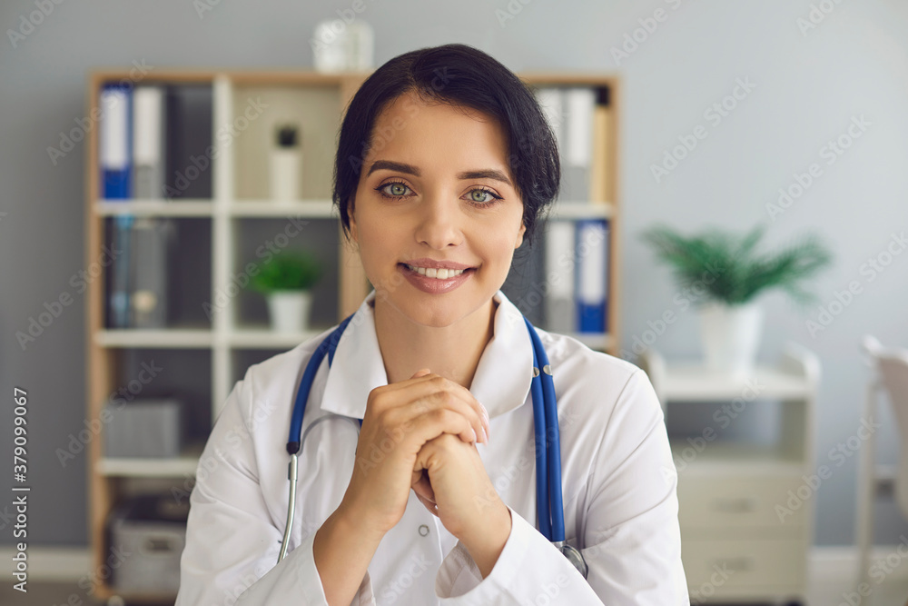 Friendly young doctor looking at camera during online consultation in her modern hospital office Friendly young doctor looking at camera during online consultation in her modern hospital office