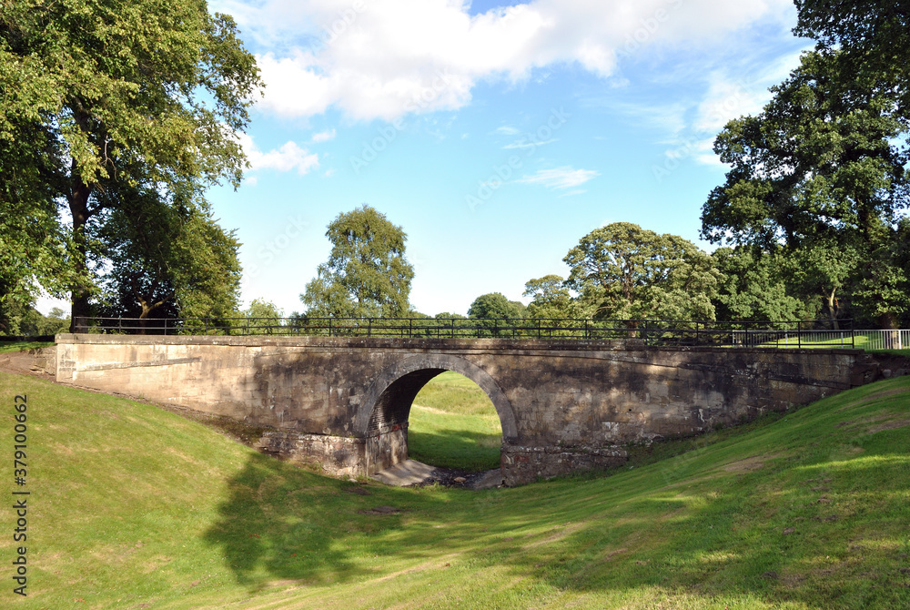 Old Stone Bridge over Dry Ditch in Public Park with Trees & Blue Sky 