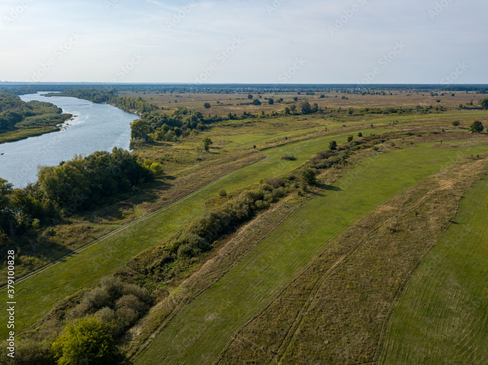 Dirt road among green meadows. Summer sunny day. Aerial drone view.