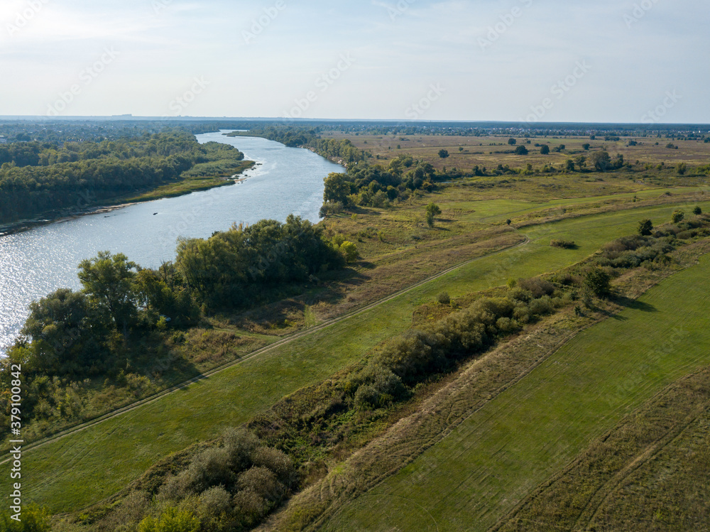 Obraz premium Dirt road among green meadows. Summer sunny day. Aerial drone view.