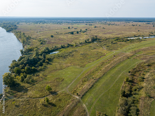 Fototapeta Naklejka Na Ścianę i Meble -  Dirt road among green meadows. Summer sunny day. Aerial drone view.