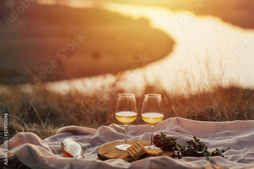 Obraz na płótnie Romantic picnic on the mountain with river and sunset on background. Bottle of wine, glasses, plaid and dessert. w salonie