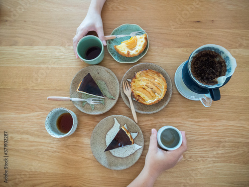Variety of sweet bakery dishes on wood table ,two hands hold cup of beverage from opposite side.Top view,Concept for food bakery and cafe.