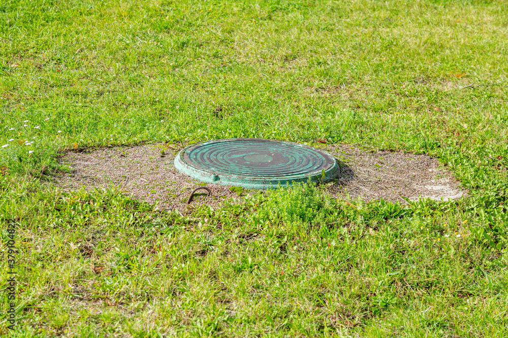 Old round manhole among lush green grass