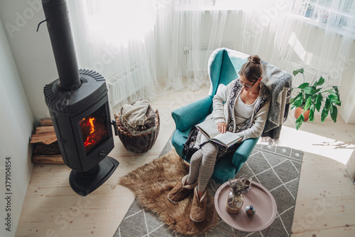 woman sitting in a cozy armchair with a warm blanket reading a book photo
