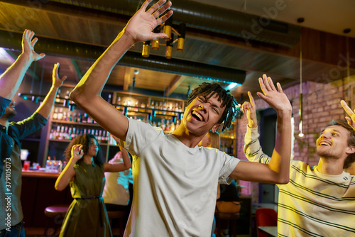 Cheerful mixed race young man having fun, dancing with friends at party in the bar