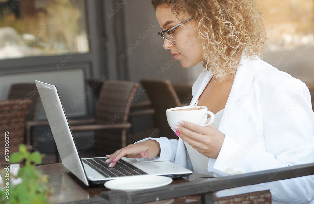 Beautiful woman drinks coffee in cafe. Distance work with laptop outdoors. Beautiful woman drinks coffee in cafe. Distance work with laptop outdoors.
