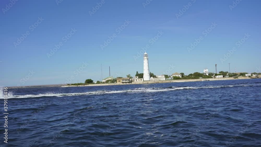 White lighthouse against the blue sea and blue sky. July 25, 2020: Crimea, Olenevka. White lighthouse against the blue sea and blue sky. July 25, 2020: Crimea, Olenevka.