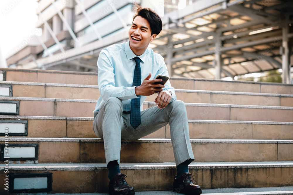 Smiling Young Asian Businessman Using Mobile Phone in the City. Sitting at the Staircase Smiling Young Asian Businessman Using Mobile Phone in the City. Sitting at the Staircase