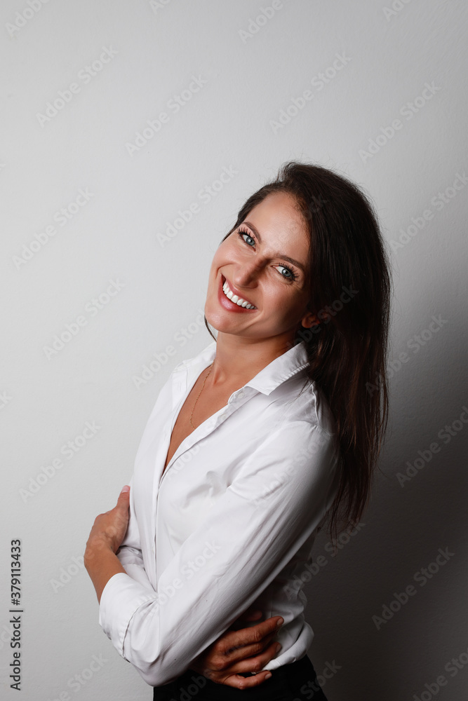 Portrait of young woman wearing white classic shirt posing isolated over grey wall background. Space for text. Portrait of young woman wearing white classic shirt posing isolated over grey wall background. Space for text.