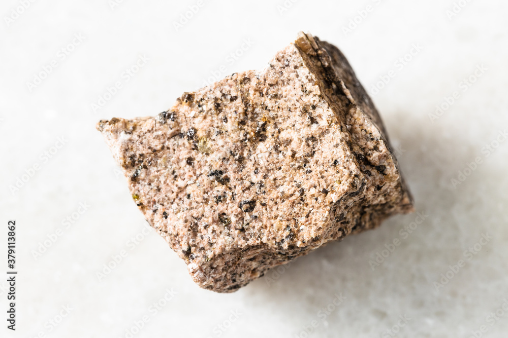 closeup of sample of natural mineral from geological collection - rough Aplite rock on white marble background closeup of sample of natural mineral from geological collection - rough Aplite rock on white marble background