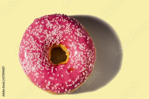 Close up view of donut sprinkled with white glaze isolated on yellow background. Food and drink concept.