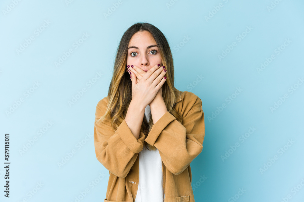 Young caucasian woman isolated on blue background shocked covering mouth with hands. Young caucasian woman isolated on blue background shocked covering mouth with hands.