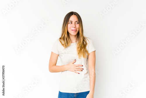 Young caucasian woman isolated on white background touches tummy, smiles gently, eating and satisfaction concept. © Asier