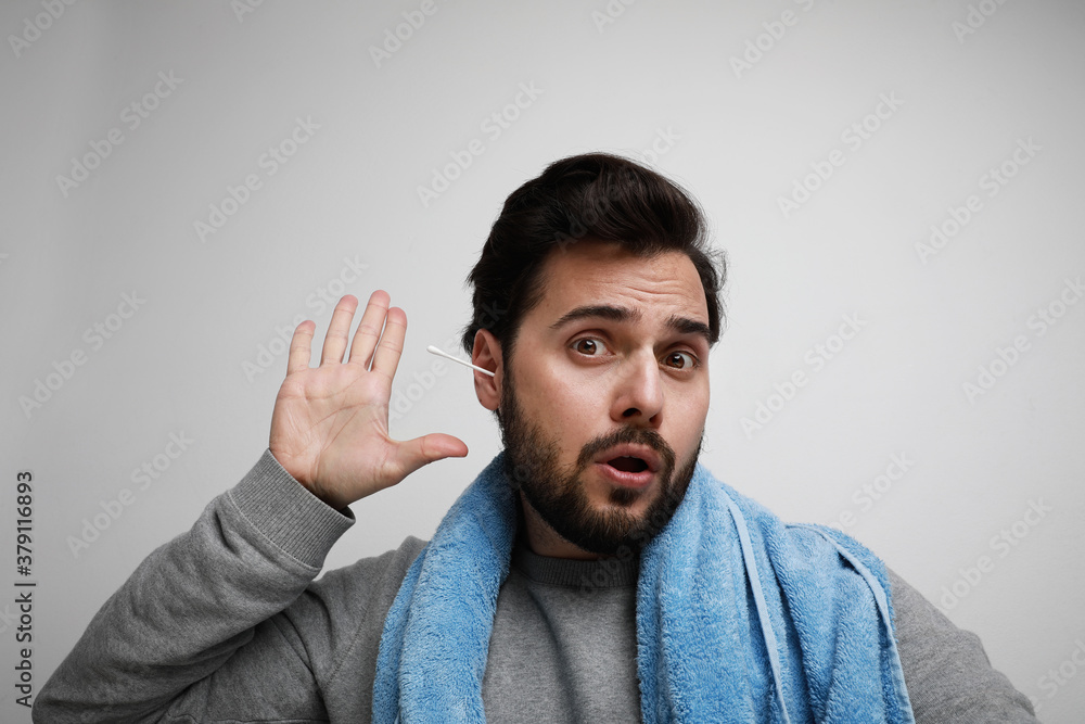 Portrait of funny bearded man cleaning his ears with blue towel, sitting over white wall. Portrait of funny bearded man cleaning his ears with blue towel, sitting over white wall.