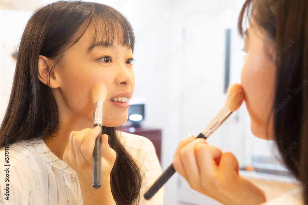 鏡の前でブラシを使いメイクをする若い女性 鏡の前でブラシを使いメイクをする若い女性
