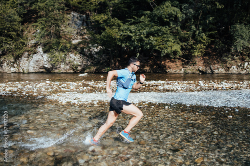 Young adult sporty man fitness and triathlon training in nature. He is running through fresh mountain river. People and extreme sports concept.