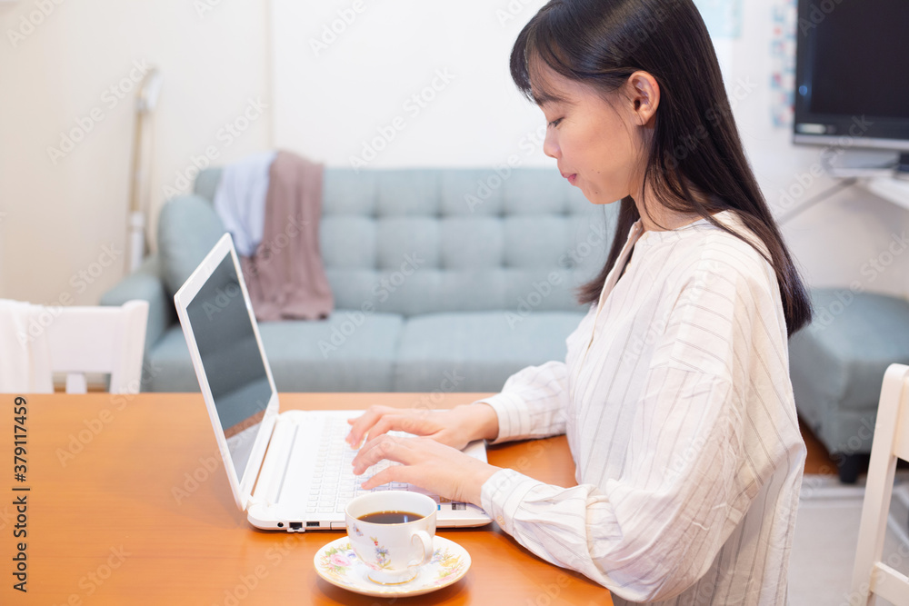 リモートワーク。自宅のキッチンテーブルでノートパソコンでの仕事中、コーヒーを飲む若く美しいビジネスウーマン。 リモートワーク。自宅のキッチンテーブルでノートパソコンでの仕事中、コーヒーを飲む若く美しいビジネスウーマン。