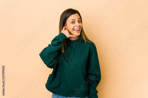 Young woman isolated on beige background showing a mobile phone call gesture with fingers. © Asier