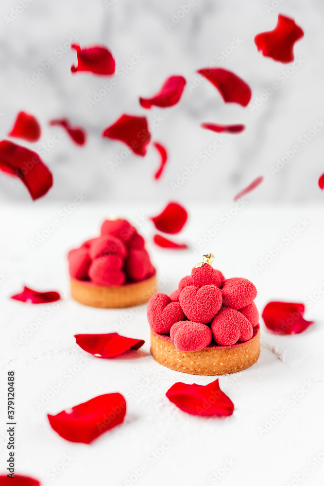 Sweet dessert tartelettes with red mousse hearts on top, decorated with red rose petals