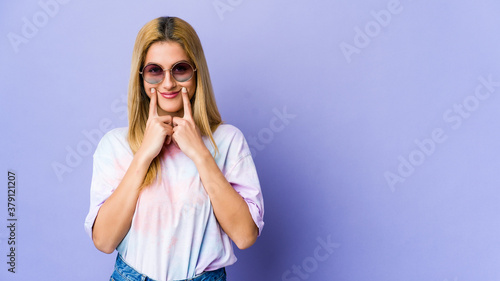 Young hipie woman with glasses isolated on purple background doubting between two options.