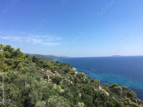 Sunny rock coast in Greece with clear sky with trees on foreground © Andrew