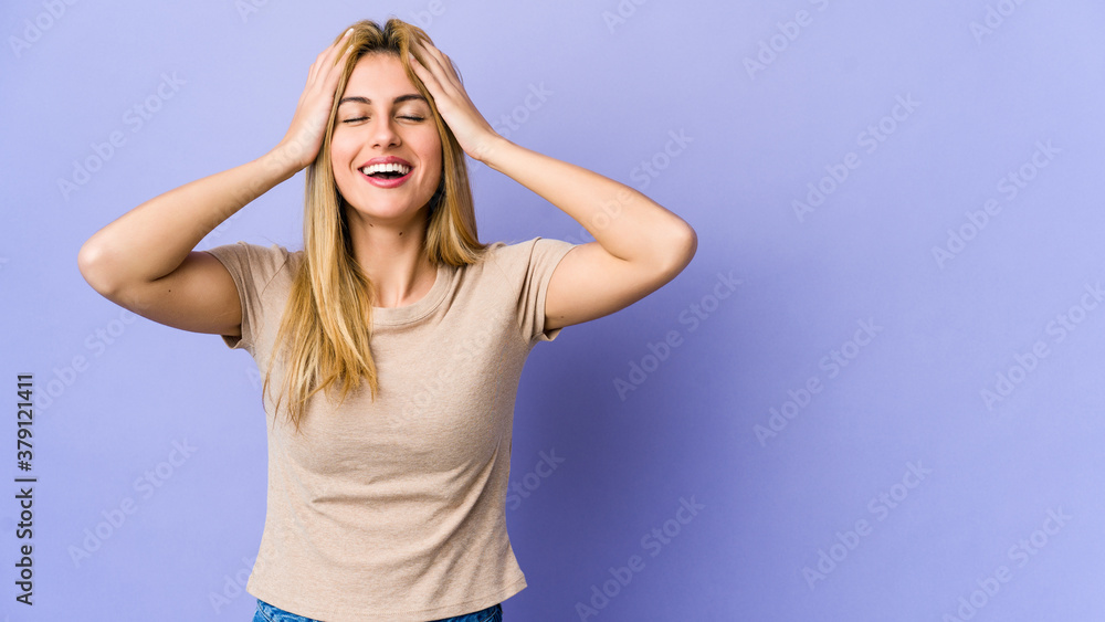 Young blonde woman isolated on purple background laughs joyfully keeping hands on head. Happiness concept. Young blonde woman isolated on purple background laughs joyfully keeping hands on head. Happiness concept.