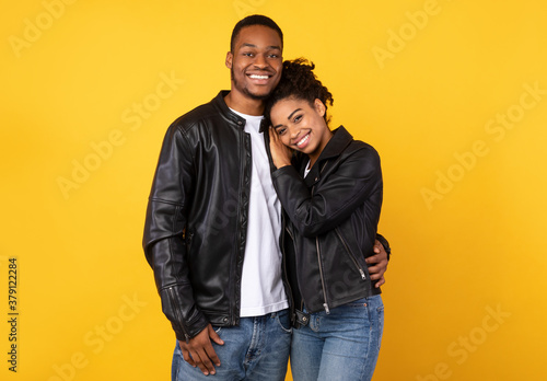 Happy Black Couple Embracing Posing Standing On Yellow Studio Background