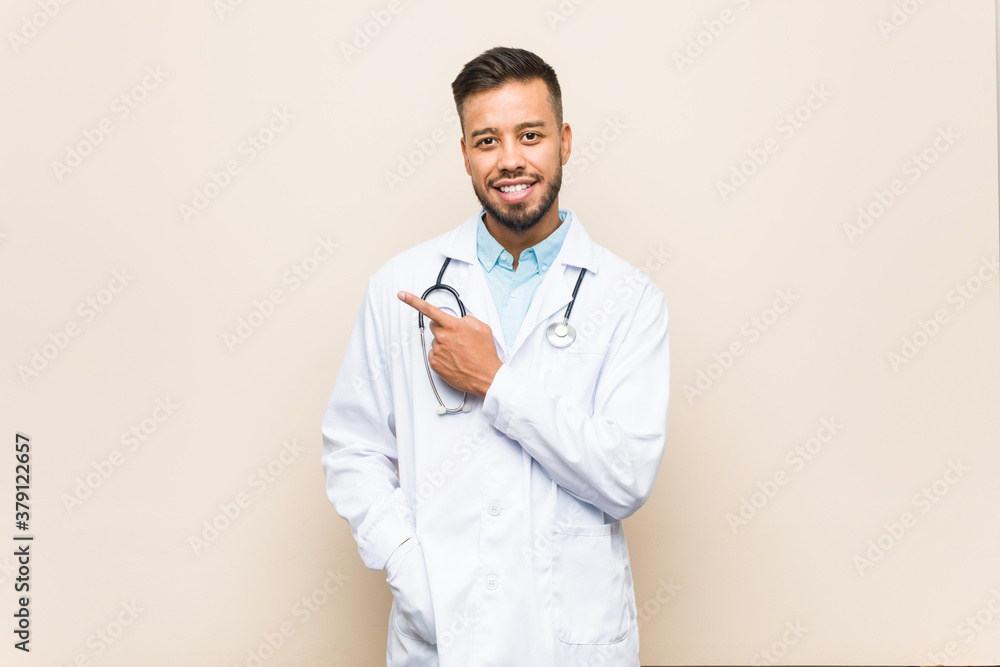 Young south-asian doctor man smiling and pointing aside, showing something at blank space. Young south-asian doctor man smiling and pointing aside, showing something at blank space.