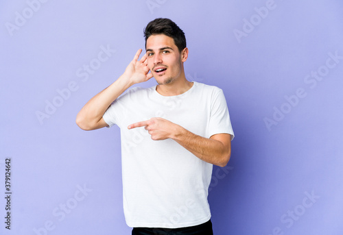 Young caucasian man isolated on purple background trying to listening a gossip.