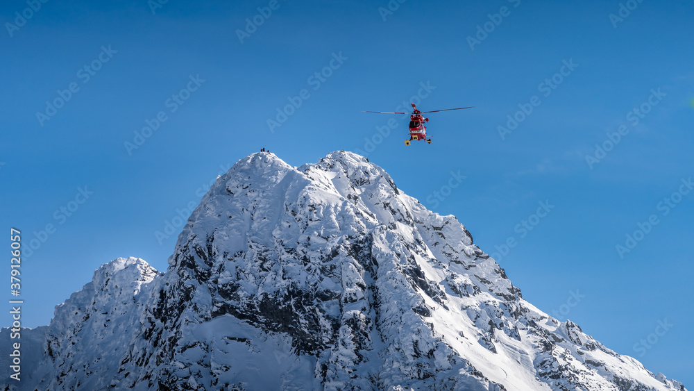Rescue helicopter saved mountain climbers. People on the top of Swinica steep and rocky mountain peak at winter, Tatra Mountains, Poland Rescue helicopter saved mountain climbers. People on the top of Swinica steep and rocky mountain peak at winter, Tatra Mountains, Poland